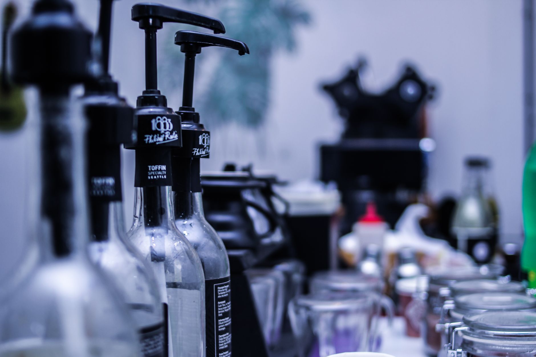 Three glass pump bottles of coffee syrup lined up beside an espresso machine