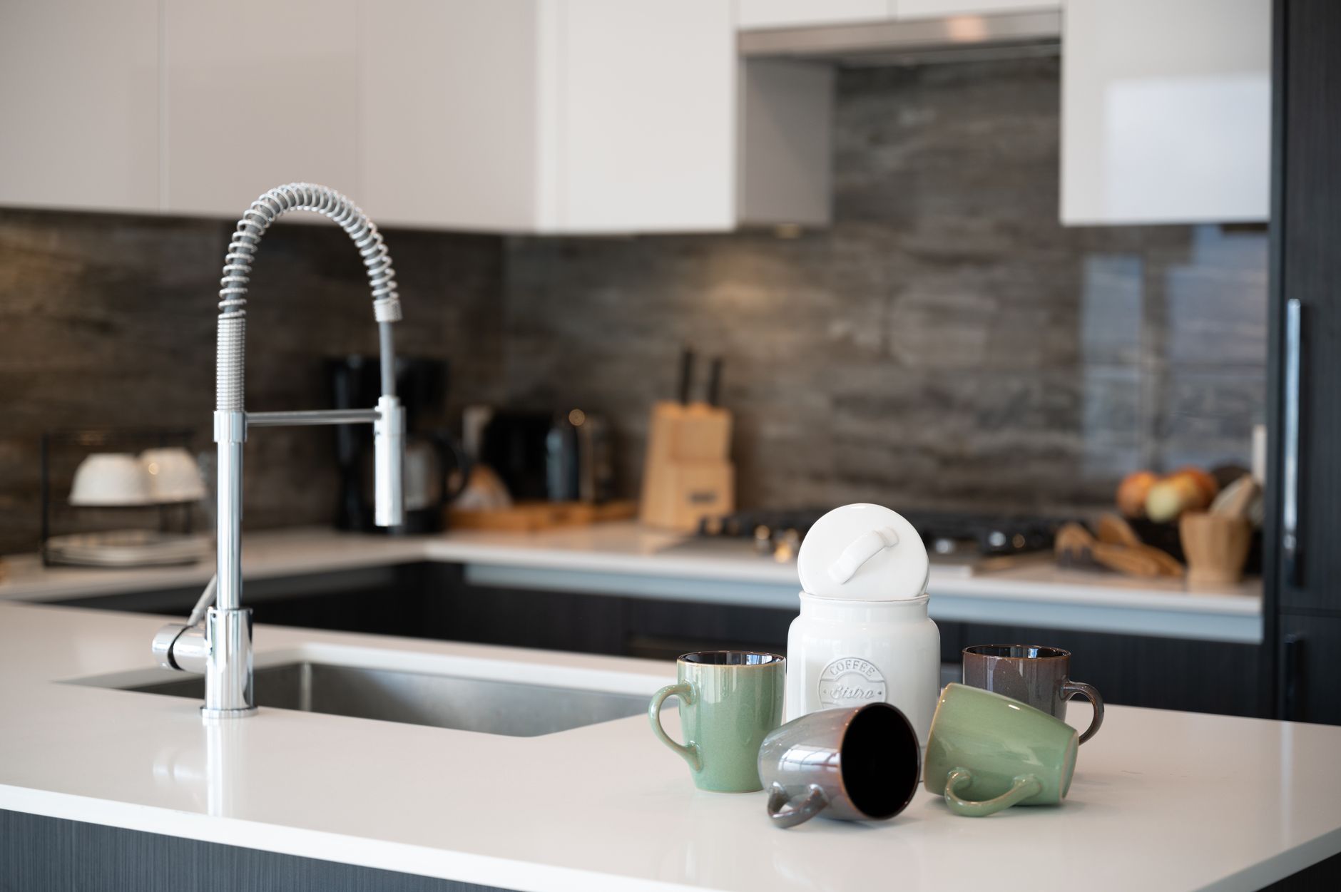 A wooden tray containing a canister, two mugs, and a small spoon rest on a kitchen counter