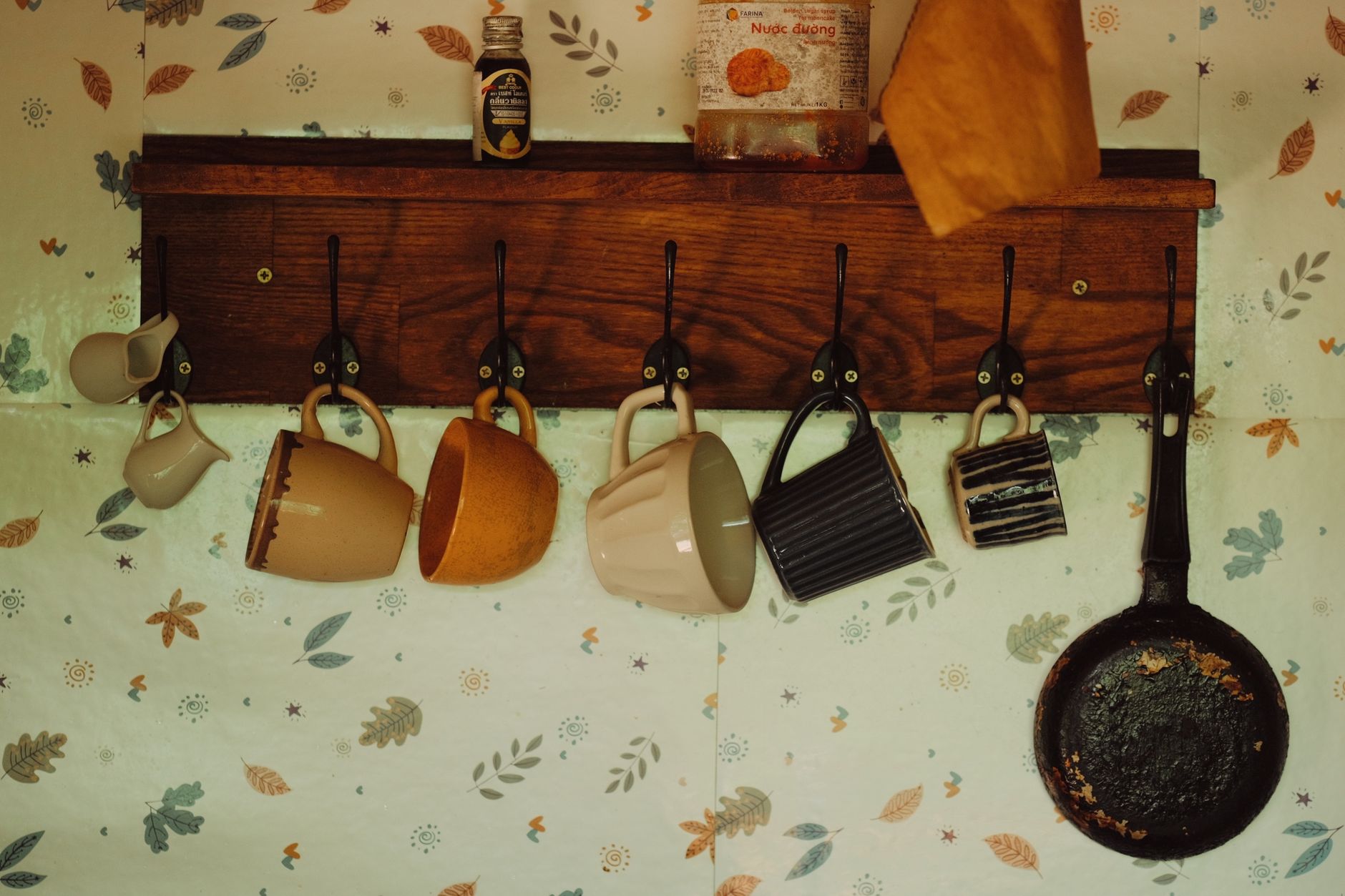 Six mugs hanging from hooks under the lip of a wooden shelf