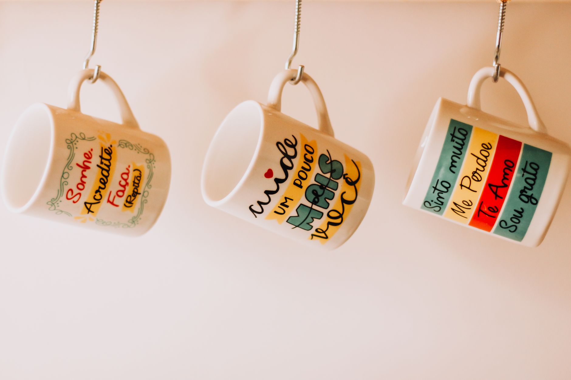 Ceramic mugs hanging from small hooks screwed into the underside of an upper cabinet