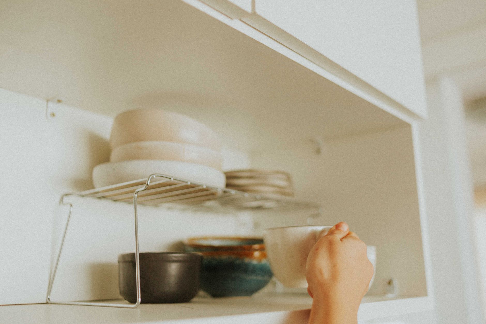 Open cabinet with baskets, stacked mugs, and a riser shelf holding coffee supplies