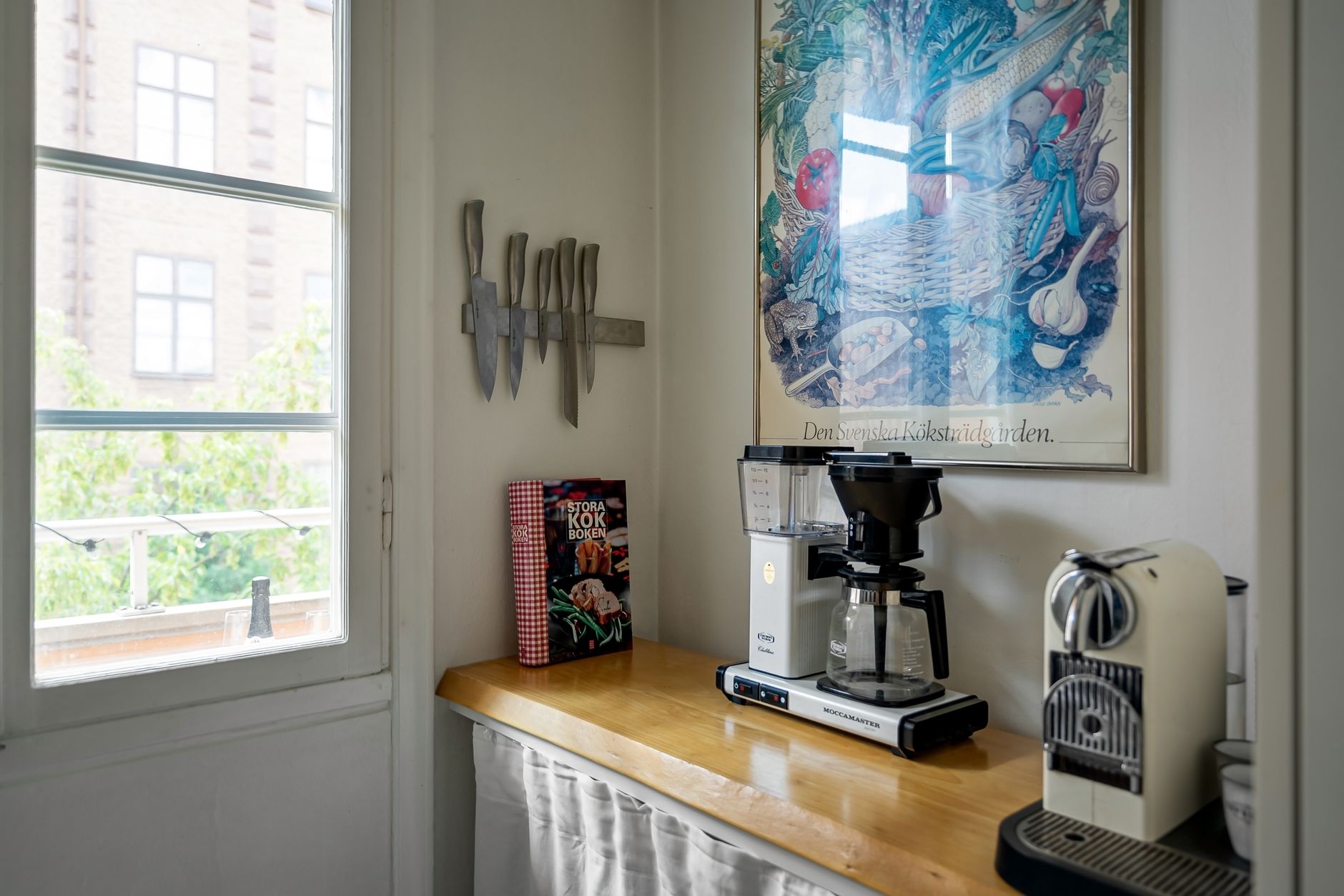 Rolling metal cart holding a coffee maker, grinder, and mugs against an apartment wall